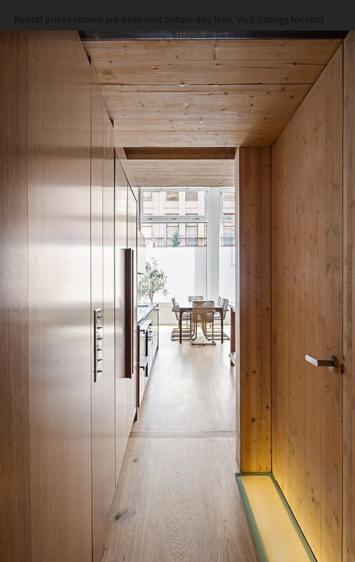 Full-height walnut storage wall along a hallway leading to a bright dining room