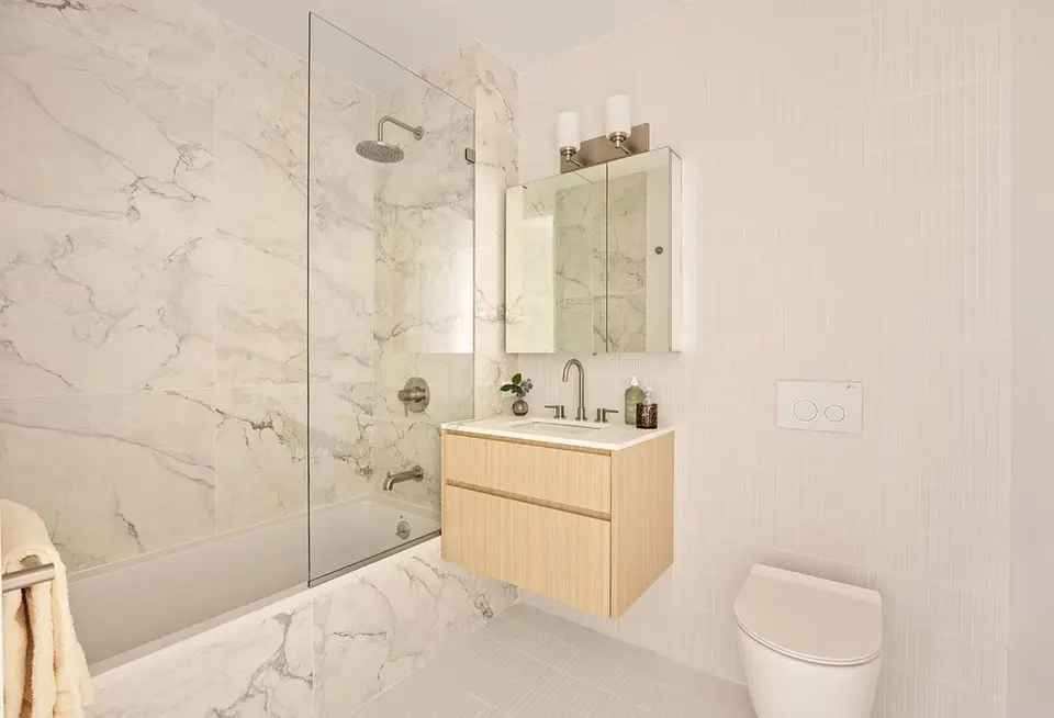 Bathroom with floating light wood vanity, marble tub wall, and medicine cabinet