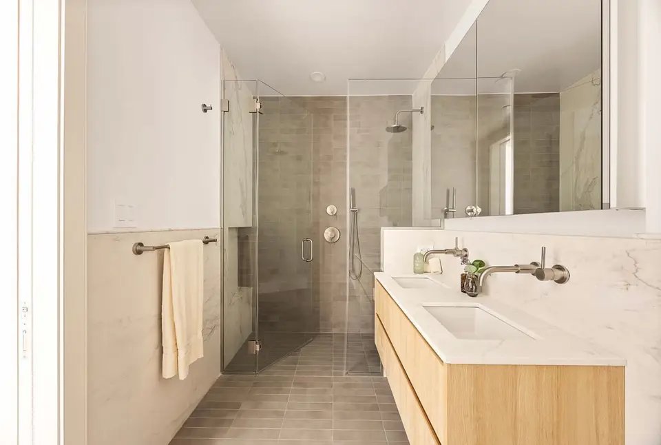 Bathroom with light wood double vanity, marble top, wall faucets, and glass shower