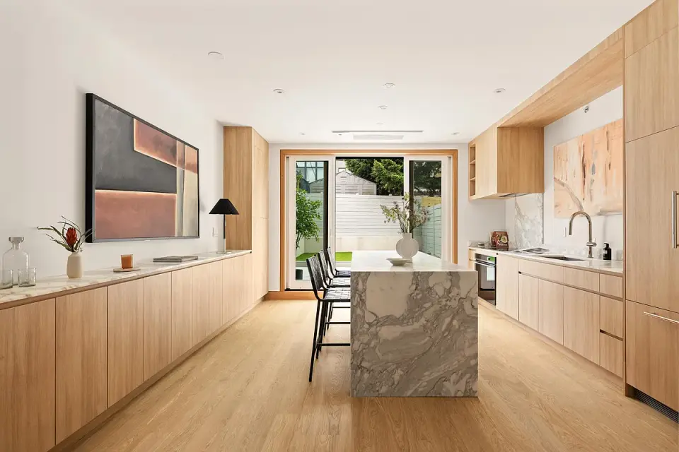 Completed modern kitchen with natural wood cabinetry and marble waterfall island