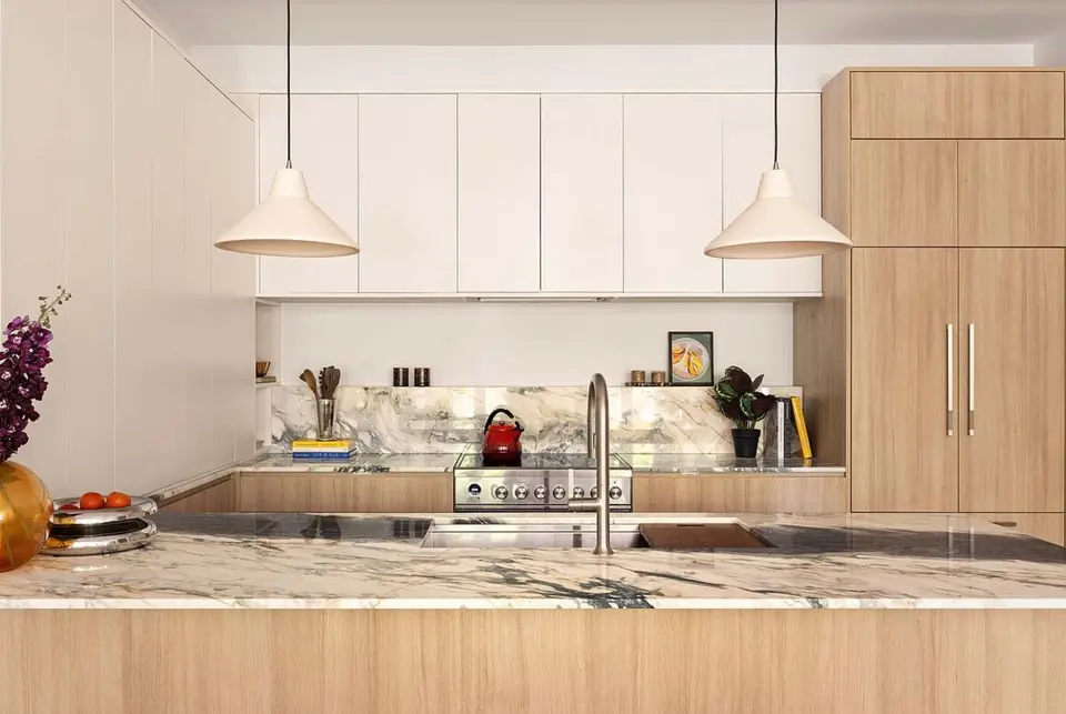 Light wood kitchen with white upper cabinets, marble peninsula and backsplash, and panel-ready fridge