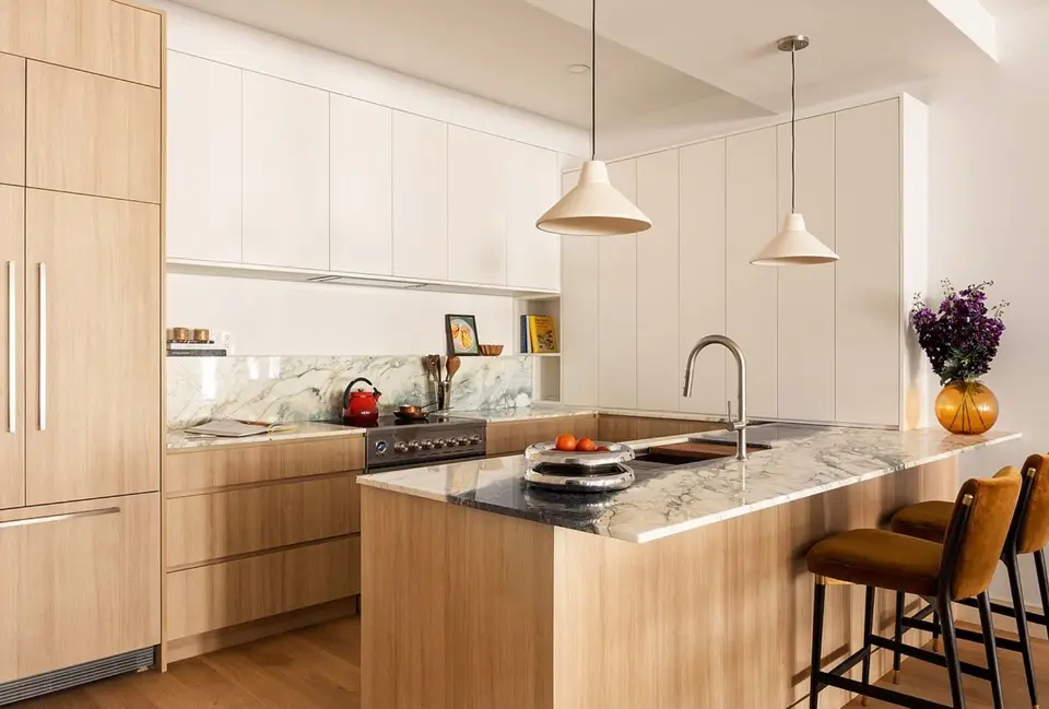 Light wood U-shaped kitchen with marble peninsula, white tall cabinets, and velvet bar stools