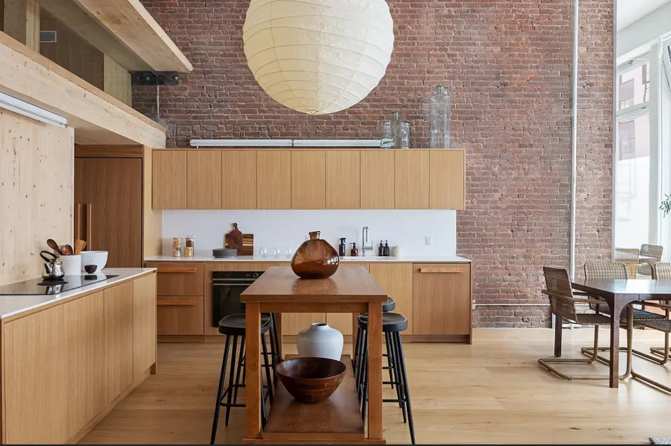 Loft kitchen with natural wood cabinetry, exposed brick wall, and pendant lighting