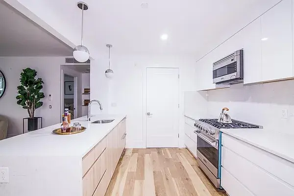 Minimalist white kitchen with wood lower island cabinets and pendant lights