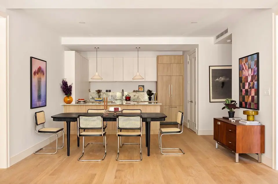 Dining room facing a white and light wood kitchen with a paneled fridge