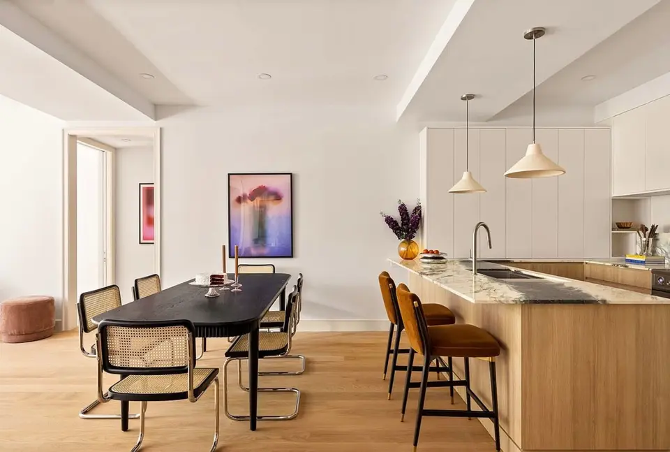 Open kitchen and dining room with light wood peninsula, marble counter, and white tall cabinets